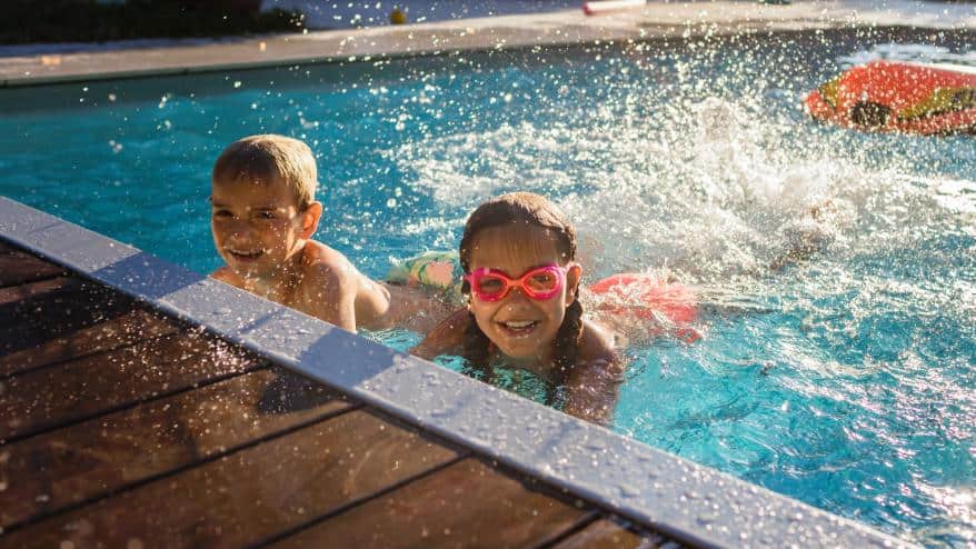 two happy children play and splash in their home swimming pool