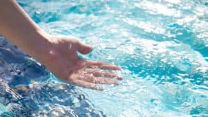 a hand runs through clear and clean pool water treated by a UV sanitizer system