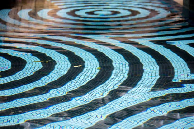 Black and white pool tiles in concentric circles seen through the surface of a pool