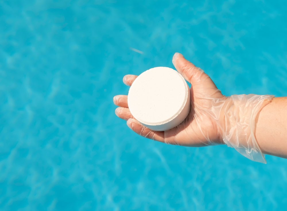 hand in protective glove holds a chlorine puck above a pool