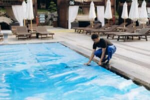Technician from a pool cleaning services company securing a thermal cover over a residential pool