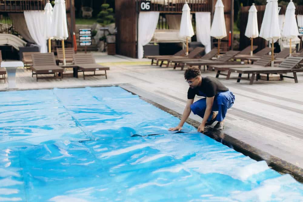 Technician from a pool cleaning services company securing a thermal cover over a residential pool