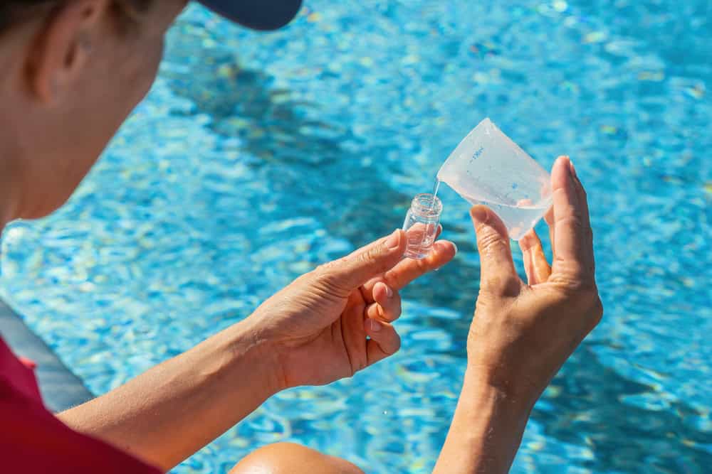 Technician dosing pool chemicals as part of how to lower alkalinity in pool safely